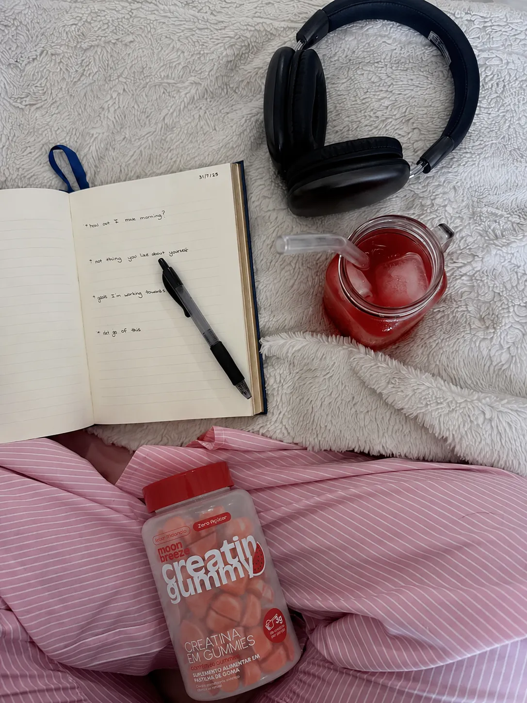 Caderno, fones e a Creatin Gummy sobre a cama