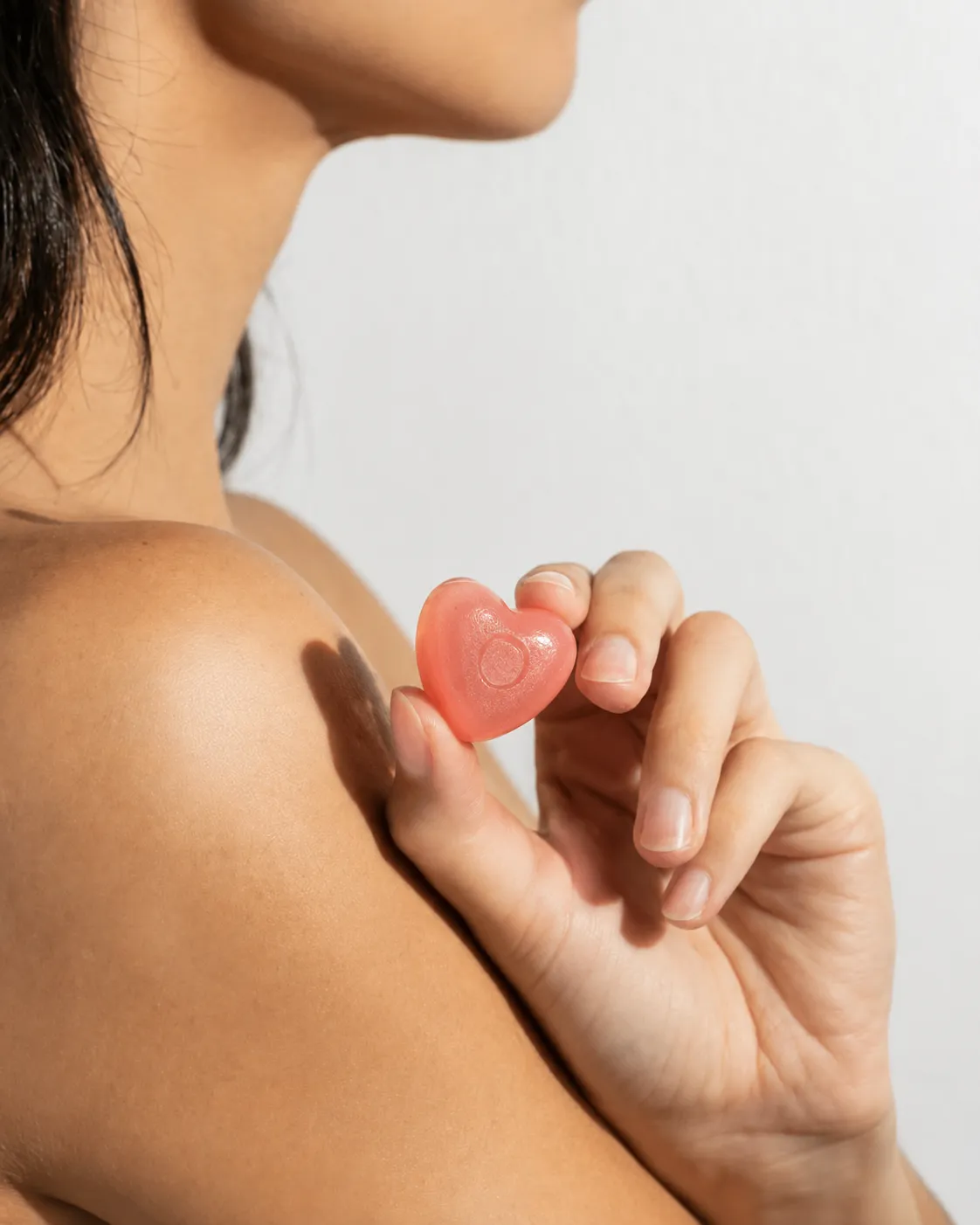Mulher segurando uma gummy em formato de coração no ombro